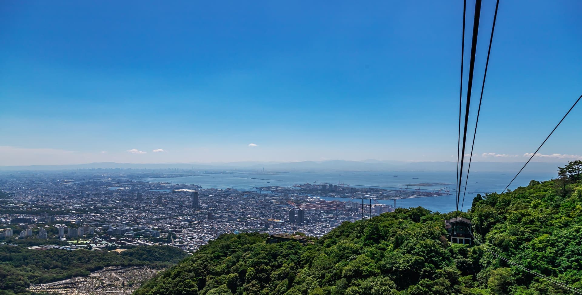 六甲山行きの急行バスから見た六甲山の緑の先には神戸の街並み。その奥には海が見えます。